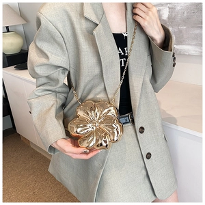Elegant gold flower evening clutch with metal chain strap worn by a model in casual blazer