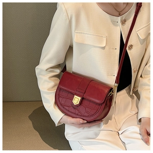 Detail of burgundy saddle bag with crocodile texture and golden shield metal buckle