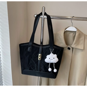 Detail of black pleated nylon tote bag with cloud charm and golden buckle on clothes rack
