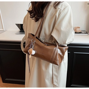 Detail of glossy brown patent leather tote bag with creative baseball charm and embossed logo