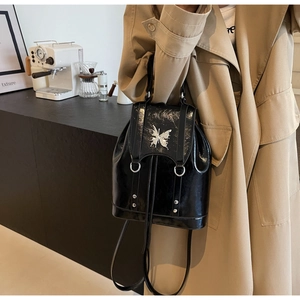 Detail of glossy black backpack with silver butterfly ornament and drawstring closure