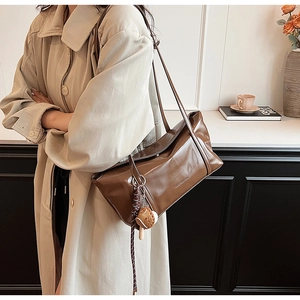Detail of glossy brown leather bag featuring an embossed logo and decorative pendant