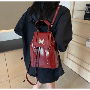 Detail of a shiny red patent leather backpack featuring a silver butterfly metal buckle