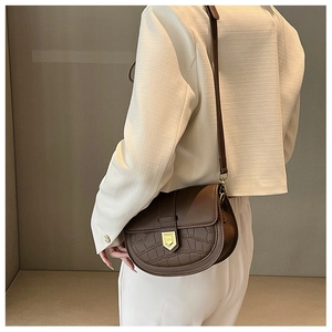 Detail of a brown saddle bag featuring crocodile texture and gold shield buckle