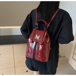 Detail of dark red patent leather backpack with silver butterfly clasp and rivet accents