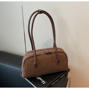 Close-up of retro brown suede baguette bag with white stitching on a book background