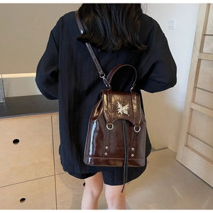 Detail of a dark brown glossy backpack with silver butterfly buckle in a home setting