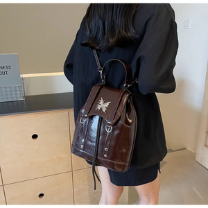 Detail of a retro dark brown glossy backpack featuring a silver butterfly metal ornament