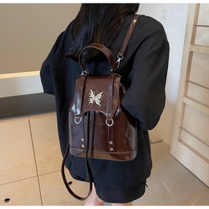 Detail of dark brown patent leather backpack featuring silver butterfly buckle detail