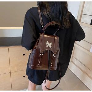 Detail of dark brown glossy leather backpack with silver butterfly metal ornament