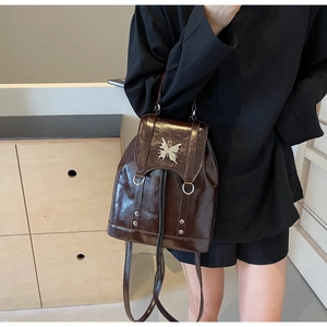 Detail of a dark brown patent leather backpack featuring a silver butterfly buckle
