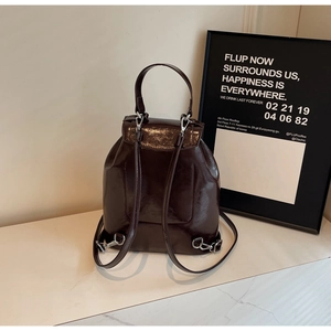 Detail of dark brown patent leather backpack with high-gloss finish and silver metal hardware