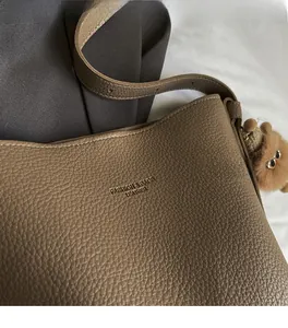 Close-up of brown litchi grain leather shoulder bag featuring a cute plush bear pendant