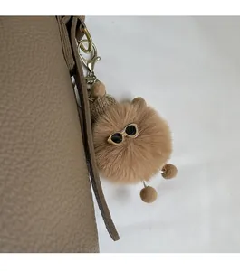 Plush brown bear keychain with sunglasses and beanie accessory on a bucket bag