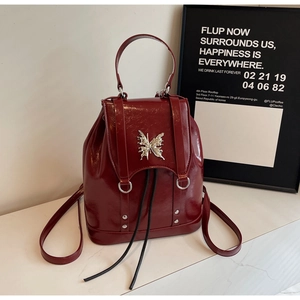 Detail view of burgundy glossy leather backpack with silver butterfly buckle on marble surface