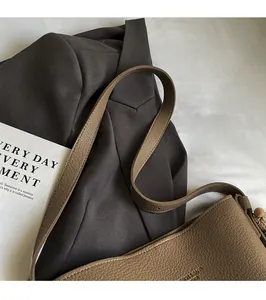 Detail of tan lychee grain leather bucket bag with gold embossed logo on white fabric