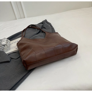 Detailed view of deep brown leather tote bag on grey blazer for a modern aesthetic