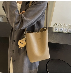 Detail of khaki bucket bag with lychee grain leather and plush doll charm on a model