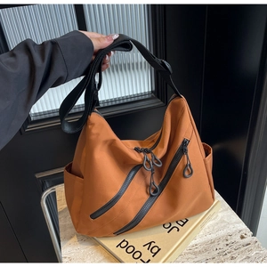 Detail of camel nylon crossbody bag showing multiple black zippers and utility style pockets