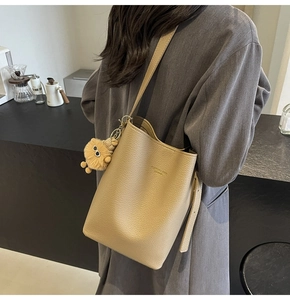 Detail view of a beige leather bucket bag with a cute plush lion charm and golden lettering