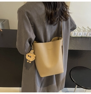 Detail of khaki pebbled leather bucket bag with plush charm on a gray blazer model
