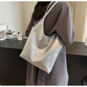 Silver metallic tote bag with geometric stitching shown on model in a cafe setting