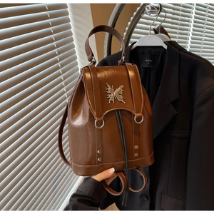 Detail of brown leather backpack featuring a vintage metal butterfly buckle and rivets