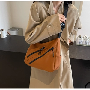 Detail of a large capacity orange nylon crossbody tote showing side pockets and wide strap