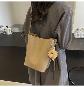 Detail view of khaki pebbled leather bucket bag with plush monster charm accessory