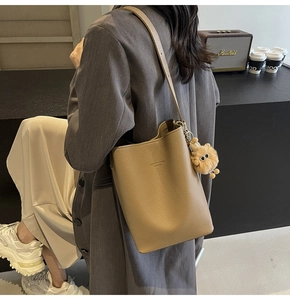 Detail of khaki pebbled leather bucket bag featuring a cute plush monster charm and logo