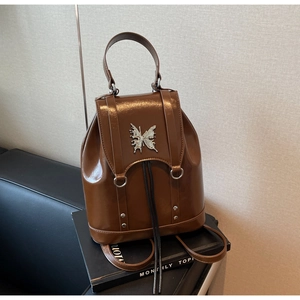 Detail of a brown patent leather backpack featuring a large silver metal butterfly buckle