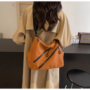 Detail of crossbody bag featuring dual diagonal zippers and wide black strap on ginger nylon