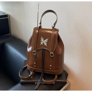 Detail of a brown glossy leather backpack featuring a silver metal butterfly logo and rivets