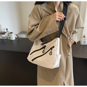 Close-up of beige nylon crossbody tote bag with wide black strap and multi-pocket design