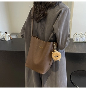 Detail of dark brown leather bucket bag with plush bear charm and pebbled texture