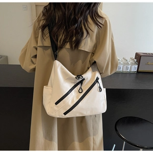Close-up of a light beige nylon crossbody bag featuring unique diagonal zippers and adjustable strap