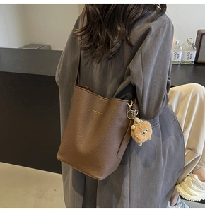 Detail of brown litchi pattern leather bucket bag with fur ball charm and shoulder strap