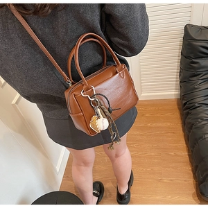Detailansicht der karamellbraunen Ledertasche mit Baseball-Anhänger und Web-Dekoration