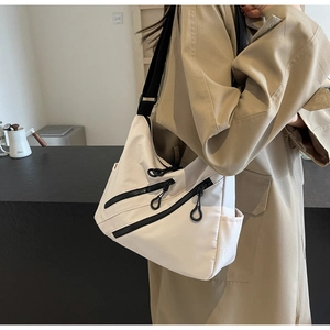 Detail of minimalist beige nylon crossbody bag with dual black zippers and adjustable strap