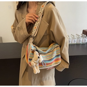 Detailed close-up of rainbow striped woven bag with puppy charm on model in trench coat