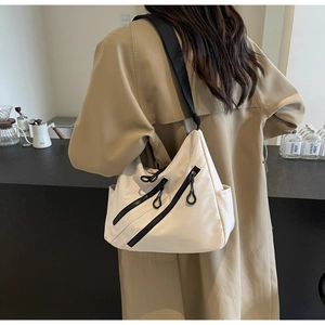 Detail of off-white nylon tote bag with wide black strap and diagonal zipper accents