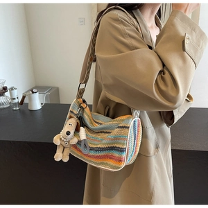 Detail of colorful rainbow woven crossbody bag featuring a plush dog charm and patterned strap
