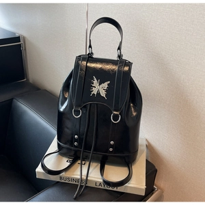 Detail of glossy black leather backpack featuring a silver butterfly buckle and studs