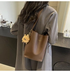 Detail view of a brown pebbled leather bucket bag with a yellow plush charm