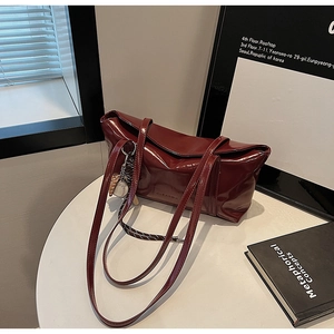 Detail of burgundy glossy oil wax leather tote bag with stylish baseball charm on white table