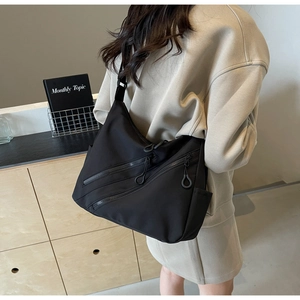 Detailed close-up of a black nylon crossbody bag featuring triple parallel zipper pockets