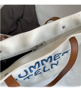 Détail d'une fermeture éclair en métal et d'une poignée en similicuir sur un cabas blanc