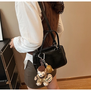 Détail du sac à main noir brillant avec poignées rondes et breloque ours en peluche