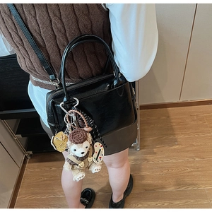 Nahaufnahme der schwarzen Lackleder-Tasche mit Rundgriffen und einem süßen Plüsch-Anhänger
