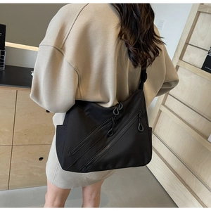 Detail of black nylon crossbody bag featuring dual diagonal zippers and matte texture